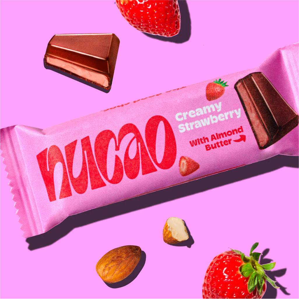 nucao Schokoriegel mit cremiger Erdbeerfüllung und Mandelbutter, umgeben von Erdbeeren und Mandeln auf pinkem Hintergrund.